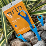 Grin tongue cleaner pouch propped among rocks and plants with several blue scrapers visible