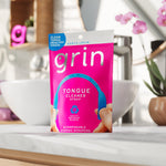 Grin Tongue Cleaner Strap pink retail pouch placed on a bathroom counter with blurred sink and plants in background