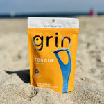 Grin orange pouch of tongue cleaner standing upright on sand with blurred beach background