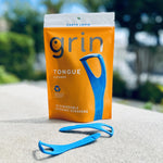 Product pouch of Grin tongue cleaner staged outdoors with two blue scrapers placed in front