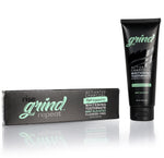 Black tube of Grind activated charcoal whitening toothpaste next to its black branded box on white reflective surface