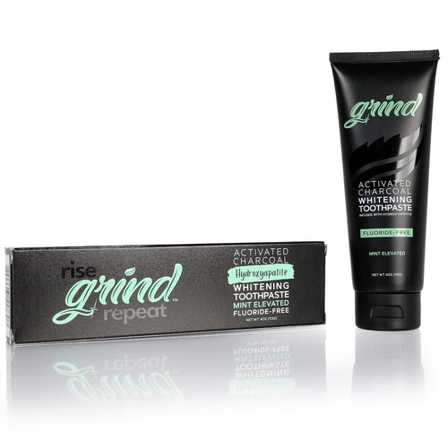 Black tube of Grind activated charcoal whitening toothpaste next to its black branded box on white reflective surface