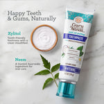Guru Nanda toothpaste tube styled on a marble surface beside a bowl of white powder and a neem leaf, with ingredient callouts.