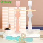 Two standing translucent Haakaa 360 baby toothbrushes and one lying on a marble platform with branded logo