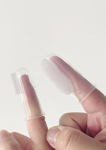 Two clear silicone finger brushes worn on adult fingers against a light background