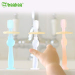 Three Haakaa translucent baby toothbrushes with suction bases lined up on a sink edge, child reaching