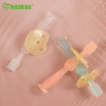 Two translucent Haakaa 360 baby toothbrushes with pacifier-style shields arranged on a pink surface
