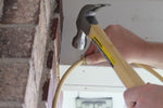 Person using a hammer to drive a U-shaped clip into an overhang to secure tan misting tubing in place.