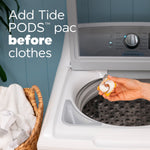 Hand placing a Tide POD into the drum of a top-loading washing machine with instruction text to add the pod before clothes.