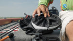 Close-up of a hand cinching the drawstring top of a Star brite mesh trash bag mounted with a suction-cup clip