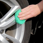 Hand using a green Scrub Daddy sponge to clean the rim of a car wheel in a close-up shot