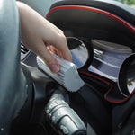 Hand holding a gray ribbed foam sponge while cleaning around a car dashboard gauge area.