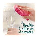 Close-up of a hand using a pink sponge to clean the rim of a stemmed glass with text noting it’s safe on stemware