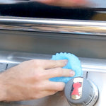 Hand using a blue Scrub Daddy sponge to clean a stainless steel stove or cooktop control area