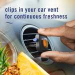 Hand clipping a Febreze Car Tropical Blend vent freshener onto a circular air vent with pineapple imagery