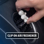 Hand clipping a small Little Joe smiling figure air freshener onto a car vent grille