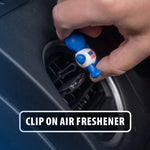 Hand clipping a small blue Little Joe vent air freshener, featuring a US flag on its torso, onto a car air vent.
