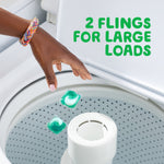 Hand dropping two green-and-white laundry pacs into top-load washing machine with text '2 flings for large loads'