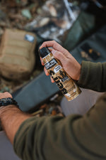 Hand holding a Ben's scent free hunting formula aerosol can over outdoor gear, label and black cap visible