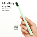 Hand holding a mint green BOKA toothbrush showing slim handle and charcoal-tipped bristles, PETA logo