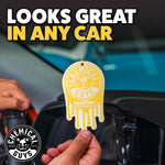 Close-up lifestyle shot of a hand holding a hanging Chemical Guys Vanilla Bean drip-shaped air freshener near a car windshield