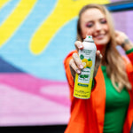 Hand-held close-up of Citrus Magic Limoncello spray can held toward camera with colorful mural background