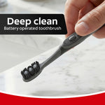 Hand holding a charcoal Colgate battery-operated toothbrush showing the soft bristle head and handle button
