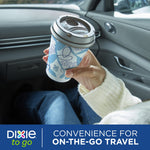 Hand holding a Dixie To Go patterned paper cup with a gray lid inside a car interior, travel lifestyle image