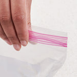 Close-up of fingers holding the pink double zipper seal of a clear resealable plastic bag
