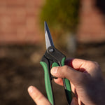 Hand-held view of green-and-black snips showing thumb on locking slider and stainless blades