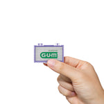 Hand holding a small translucent purple G·U·M wax case with visible logo and white wax pieces inside.