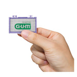Hand holding a small translucent purple G•U•M wax case showing pre-cut wax and the G•U•M logo, white background