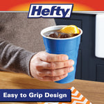 Hand holding a blue Hefty party cup filled with iced beverage, kitchen background visible