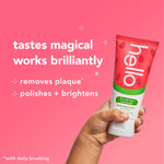 Hand holding a Hello fresh watermelon toothpaste tube against a pink backdrop with text highlighting plaque removal and brightening benefits.
