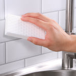 Hand holding a white melamine cleaning eraser against subway tile near a sink