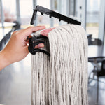 Hand holding a black mop clamp securing a white cotton mop head in an indoor setting with windows in background
