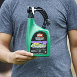 Hand holding a green Ortho WeedClear bottle in front of a person wearing a gray shirt, product label clearly visible