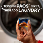 Hand holding a blue-and-orange Persil laundry pac in front of a washing machine with usage text above
