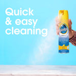Hand holding a Pledge Clean It lemon multisurface spray can against a blue background with 'Quick & easy cleaning' text