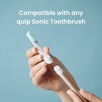 Hand holding a Quip brush head above a toothbrush handle with text stating compatibility with any Quip Sonic Toothbrush
