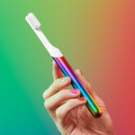 Hand holding a rainbow-metal quip sonic toothbrush against a colorful gradient background