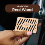 Hand holding a rectangular real-wood car air freshener with diagonal vent slots and branding callout