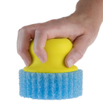 Hand gripping a yellow Scrub Hub handle attached to a blue textured round scrub pad against white background