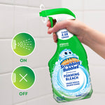 Hand holding a Scrubbing Bubbles Foaming Bleach spray bottle aimed at tiled bathroom wall, showing on/off spray icons