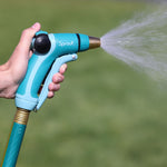 Hand holding a Sprout front-trigger nozzle spraying a fine jet of water against grassy background