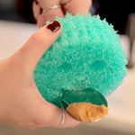 Hand holding a teal Scrub Daddy sponge scooping peanut butter from a spoon in a close-up shot