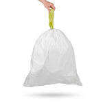 Hand holding a tied white trash bag by its green drawstring, bag suspended against a white background with soft shadow