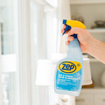 Hand gripping a Zep Air & Fabric Odor Eliminator spray bottle in a bright home interior, label clearly visible.