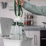 Hand lifting tied drawstring Matter compostable bag out of a small kitchen bin, handles visible