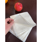 Hand lifting a white textured napkin from a stack on a dark countertop with a red apple nearby